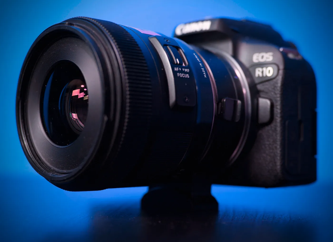 Canon EOS R10 mirrorless camera body with a lens attached, on a blue background